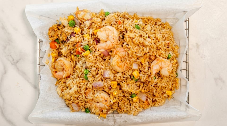 Shrimp fried rice with peas, carrots, corn, and onions in a white paper-lined basket.