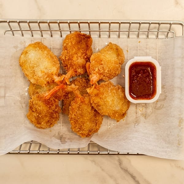 Golden brown fried shrimp with tails on, served on a metal rack with a side of dipping sauce.