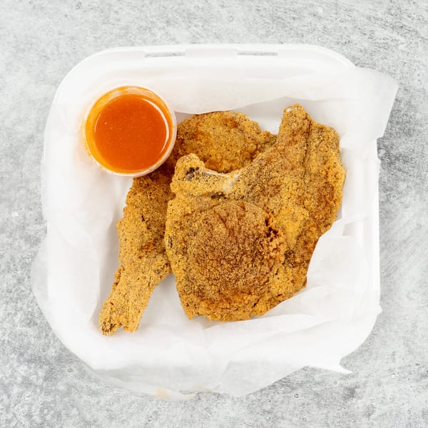 Fried fish fillets and a cup of dipping sauce in a white takeout container.