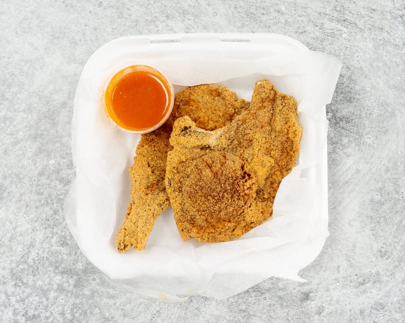 Fried fish fillets and a cup of dipping sauce in a white takeout container.