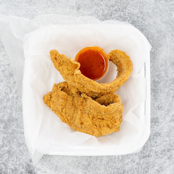 Two pieces of fried catfish and a small cup of red dipping sauce in a white takeout container.