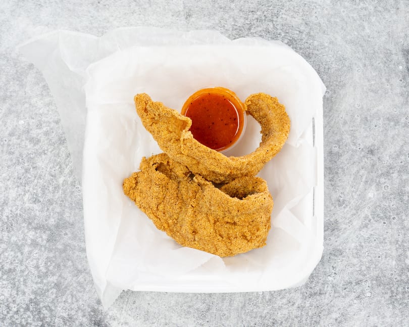 Two pieces of fried catfish and a small cup of red dipping sauce in a white takeout container.