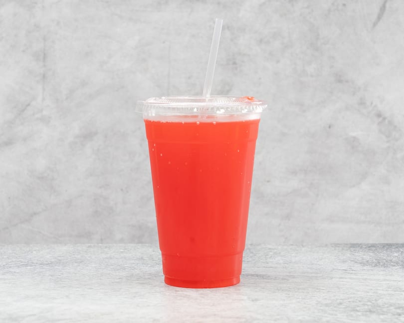 Bright red beverage in a clear plastic cup with a straw, against a gray background.