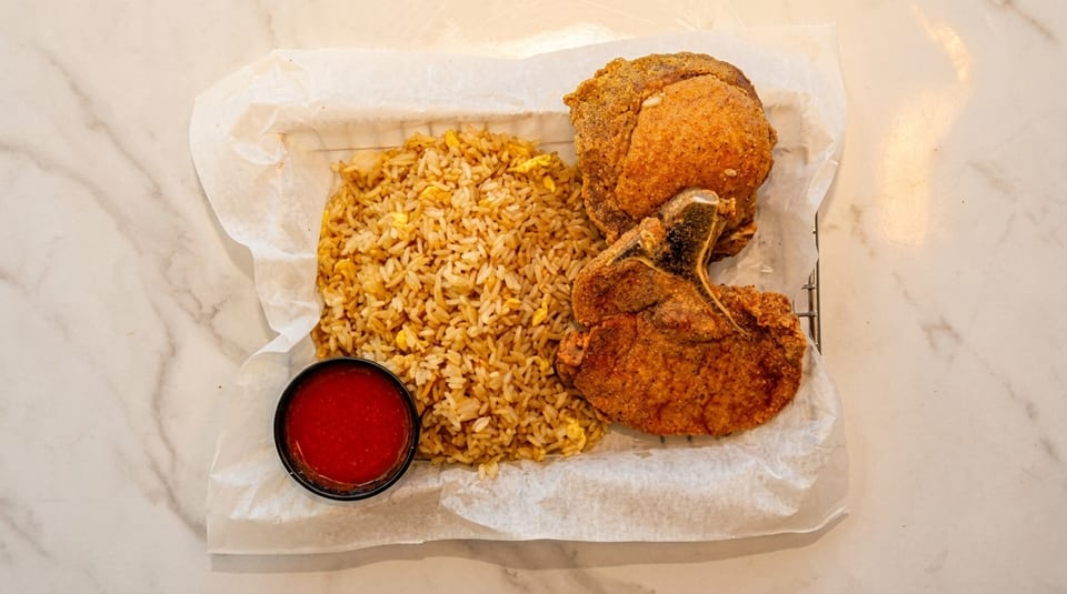 Two crispy fried pork chops with a side of fried rice and red dipping sauce.