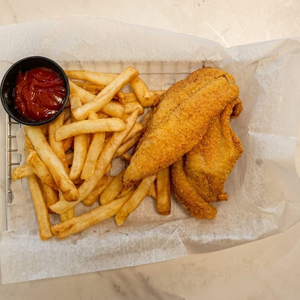 Fried fish fillets and french fries with a side of ketchup in a metal basket.