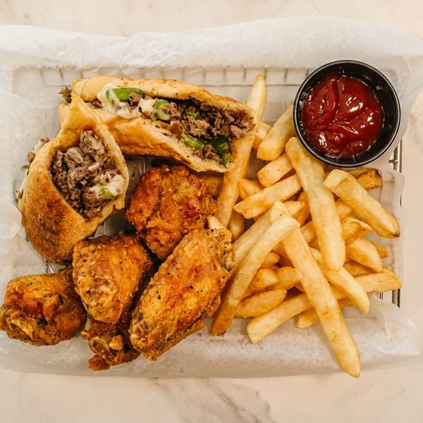 Cheesesteak egg rolls, fried chicken wings, and french fries with ketchup in a basket.