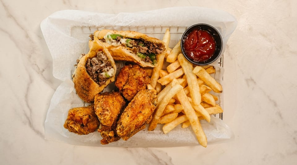 Cheesesteak egg rolls, fried chicken wings, and french fries with ketchup in a basket.