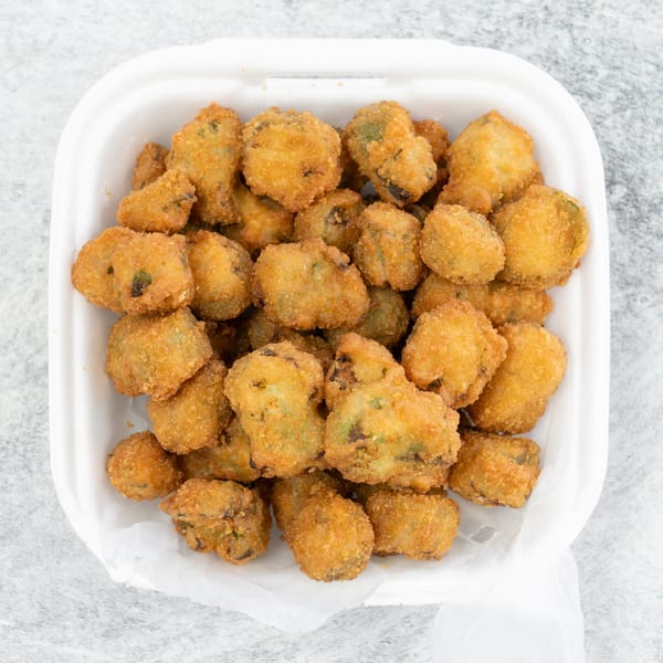 A white takeout container filled with golden-brown fried okra pieces on a light gray surface.