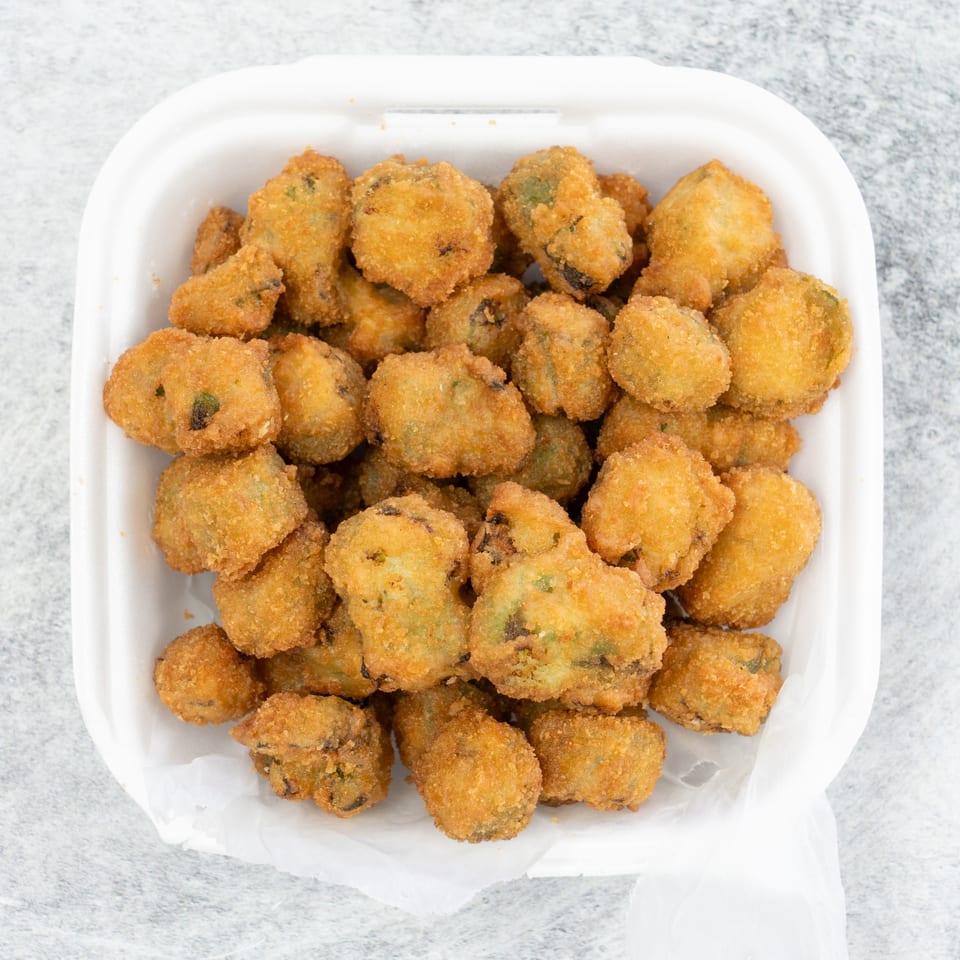 A white takeout container filled with golden-brown fried okra pieces on a light gray surface.
