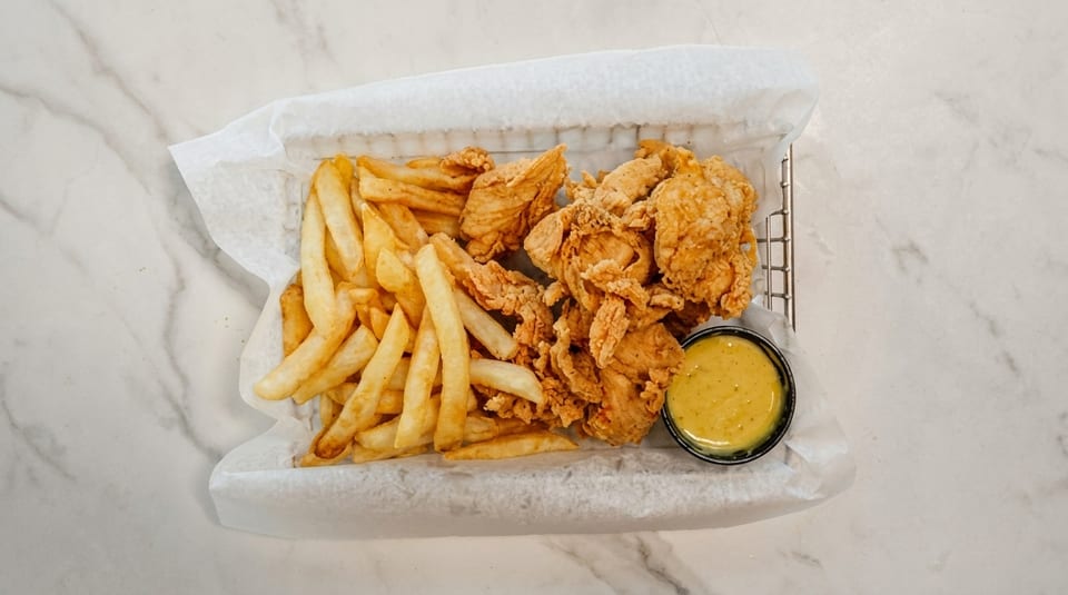 Crispy fried chicken tenders and golden french fries served in a basket with a side of dipping sauce.