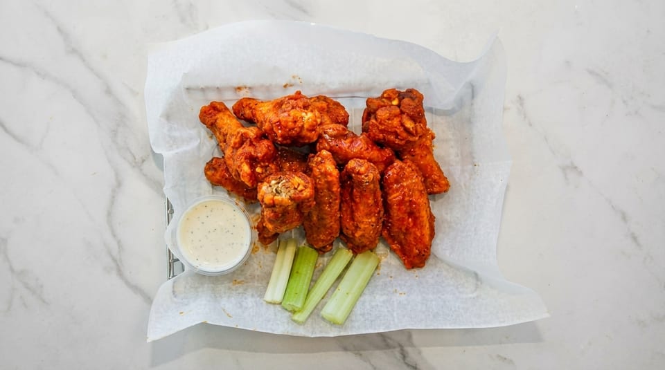 Spicy buffalo wings with ranch dressing and celery sticks on a white marble surface.
